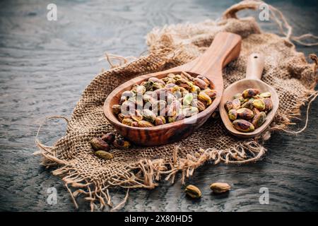 Pistacchi arrostiti e sbucciati in cucchiai di legno su fondo di legno Foto Stock