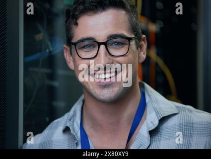 Ritratto, sorriso e supporto con un ingegnere informatico nella sala server per la manutenzione dell'infrastruttura o del mainframe. Sicurezza informatica, database e rete Foto Stock