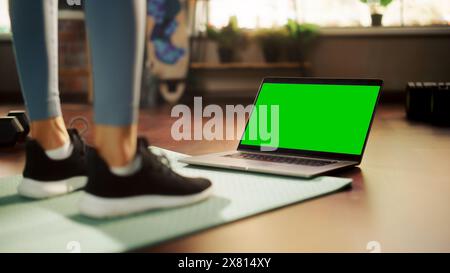 Allenamento femminile, guardare Trainer su un notebook, tramite video tutorial online con Chroma Green Screen. Atletica che utilizza l'abbonamento fitness ai servizi di streaming. Ripresa in basso di gambe e notebook Foto Stock