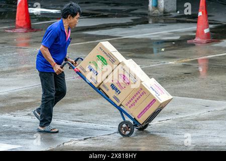 SAMUT PRAKAN, THAILANDIA, 07 MAGGIO 2024m Un uomo spinge un carrello carico di scatole sotto la pioggia Foto Stock