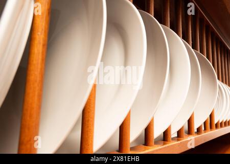 Un rack in legno con molte piastre bianche. Le piastre sono impilate in modo ordinato e ordinato Foto Stock