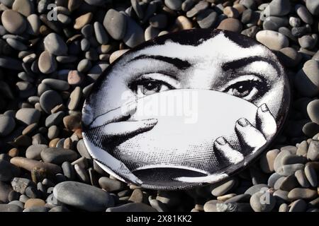 Piatto Fornasetti sulla spiaggia di ciottoli, il volto appartiene alla cantante lirica italiana Lina Cavalieri Foto Stock