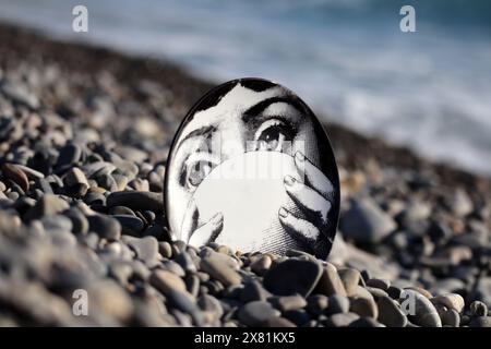 Piatto Fornasetti sulla spiaggia di ciottoli, il volto appartiene alla cantante lirica italiana Lina Cavalieri Foto Stock