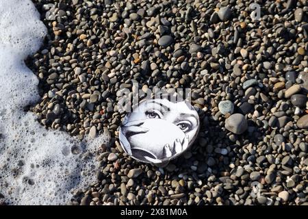 Piatto Fornasetti sulla spiaggia di ciottoli, il volto appartiene alla cantante lirica italiana Lina Cavalieri Foto Stock