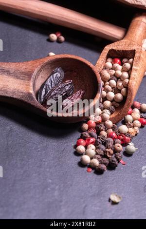 Tonka Beans e diversi tipi di grani di pepe in un cucchiaio di legno Foto Stock