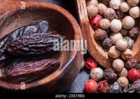 Tonka Beans e diversi tipi di grani di pepe in un cucchiaio di legno Foto Stock