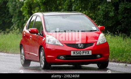 Stony Stratford, Regno Unito - 22 maggio 2024: 2010 auto Honda Jazz rossa che guida su una strada britannica in una giornata di pioggia Foto Stock