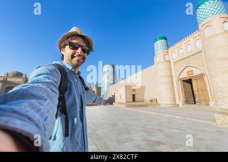 Uomo che fa un selfie con gli edifici orientali nell'antica città di Itchan Kala sullo sfondo. Khiva, Uzbekistan Foto Stock
