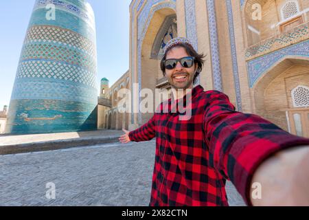 Uomo che fa un selfie con gli edifici orientali nell'antica città di Itchan Kala sullo sfondo. Khiva, Uzbekistan Foto Stock