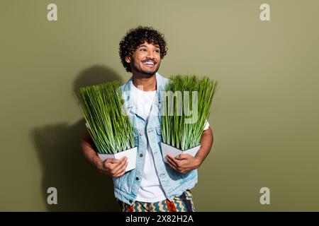 Foto ritratto di un bel giovane uomo tenere l'erba sembra uno spazio vuoto vestito elegante indumento in denim isolato su sfondo color cachi Foto Stock