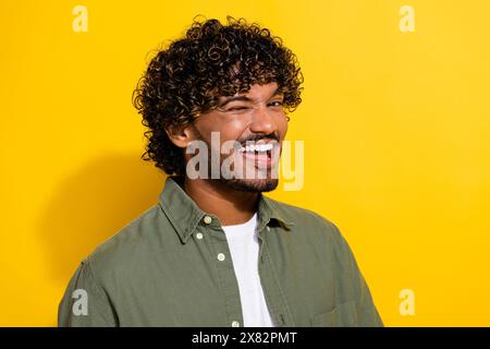 Foto ritratto di un giovane e attraente ispanico in camicia cachi che lampeggia l'occhio e flirta con te isolato su sfondo giallo Foto Stock