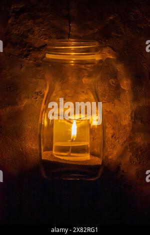 Una candela accesa in una lanterna illumina lo sfondo scuro con una fiamma ardente Foto Stock