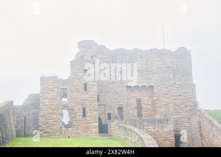 Una vista nebbiosa di un antico castello in pietra con mura parzialmente crollate e un primo piano erboso. Foto Stock