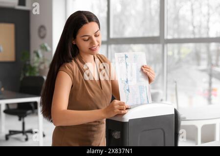 Giovane segretaria che distrugge i documenti usando il tritadocumenti in ufficio Foto Stock