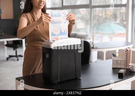 Giovane segretaria che distrugge i documenti usando il tritadocumenti in ufficio Foto Stock