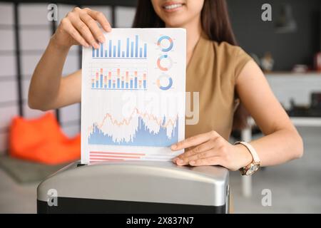 Giovane segretaria che distrugge documenti usando il trituratore in ufficio, primo piano Foto Stock