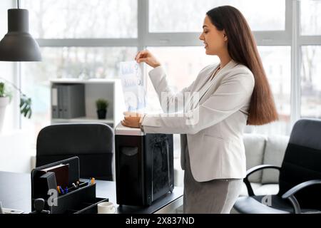 Giovane segretaria che distrugge i documenti usando il tritadocumenti in ufficio Foto Stock