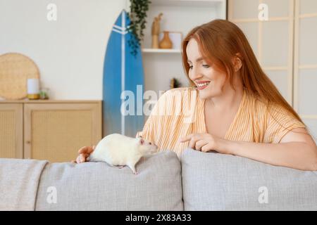 Bella donna rossa con un topo bianco carino sul divano a casa Foto Stock