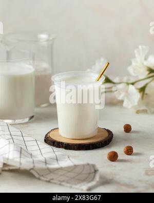 Yogurt fresco in una tazza di plastica con un cucchiaio dorato su un rustico sottobicchiere in legno. Prodotto lattiero-caseario Foto Stock