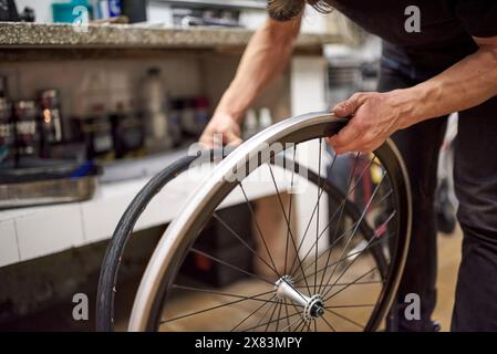 Riparatore di biciclette ispanico che installa uno pneumatico pieno senza aria su una ruota da bici in un'officina di riparazione. Composizione selettiva della messa a fuoco con spazio di copia. Foto Stock