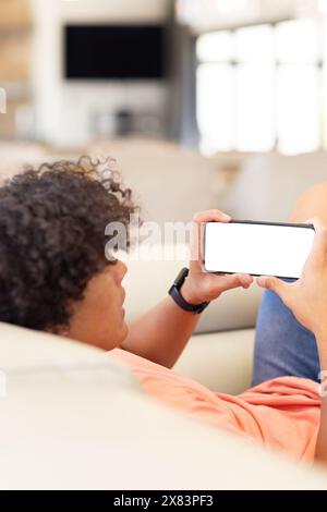 Un giovane maschio birazziale a casa, che tiene lo smartphone sul divano, copia spazio Foto Stock