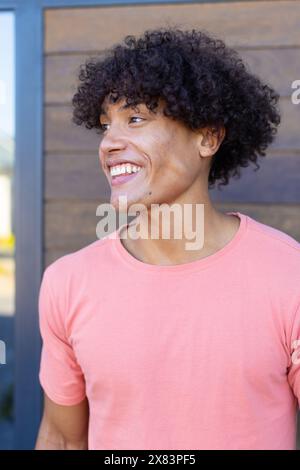 Un giovane uomo birazziale che indossa una camicia rosa e sorride all'aperto Foto Stock