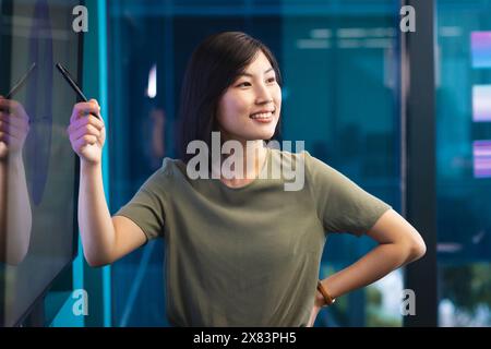 Nel moderno ufficio per gli affari, giovane donna asiatica che tiene la penna e punta lo schermo Foto Stock