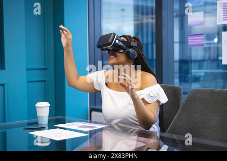 In un ufficio moderno per lavoro, donna birazziale con trecce scure e occhi marroni che utilizzano il visore VR Foto Stock