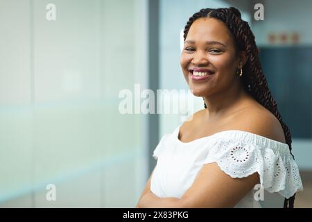 Nel moderno ufficio per gli affari, la giovane donna birazziale con lunghi capelli intrecciati sorride, copia spazio Foto Stock