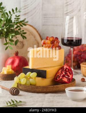 Elegante tagliere di formaggi con una varietà di formaggi, uva e accompagnamenti, abbinati a bicchieri di vino rosso Foto Stock