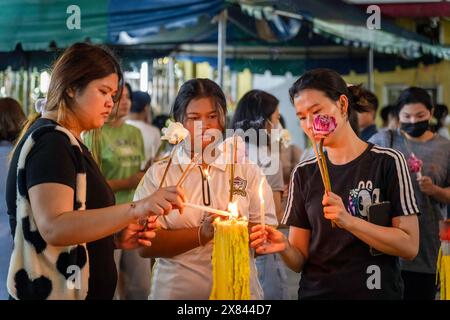 Bangkok, Thailandia. 22 maggio 2024. Un gruppo di giovani donne thailandesi ha visto accendere candele, il giorno Visakha Bucha, al Tempio Lat Phrao, situato in una comunità a basso reddito, a Bangkok, Thailandia. Visakha Bucha, una delle più importanti festività buddiste della Thailandia, commemora la nascita, l'illuminazione e il passaggio del Buddha Gautama, tutti nella stessa data. I buddisti thailandesi visitano in genere i templi per fare il merito, che comporta attività come dare l'elemosina ai monaci, ascoltare sermoni e partecipare a vari rituali religiosi. Credito: SOPA Images Limited/Alamy Live News Foto Stock