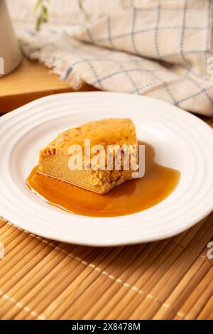 dessert di flan fatto in casa, noto anche come creme caramel, budino di crema pasticcera al caramello o crema pasticcera all'uovo, servito su un piatto bianco su un tavolo di legno. Foto Stock
