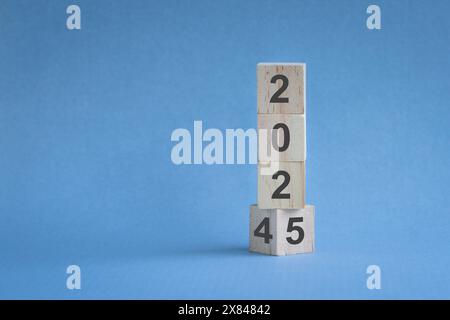 Da 2024 a 2025, numeri su blocchi di legno verticali. Su sfondo blu, concetto di anno nuovo. Foto Stock