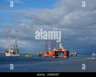 Diverse piattaforme di trivellazione petrolifera si trovano nel mare calmo sotto un cielo blu, una piccola barca è visibile in primo piano, carri di perforazione in rosso Foto Stock