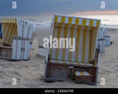 Sdraio vuoto con strisce gialle e bianche sulla spiaggia, con mare calmo sullo sfondo, colorate sdraio su una spiaggia di fronte a un buio Foto Stock