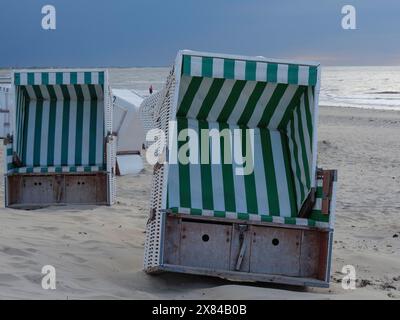 Due sdraio vuote con motivi a strisce verdi e bianche che si trovano su una spiaggia sabbiosa all'alba, atmosfera tranquilla, sedie da spiaggia colorate su una spiaggia Foto Stock