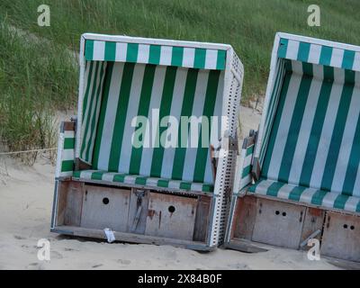 Due sedie a sdraio a righe verdi in piedi l'una accanto all'altra su una spiaggia sabbiosa di fronte alle dune, colorate sedie a sdraio su una spiaggia di fronte a un buio Foto Stock