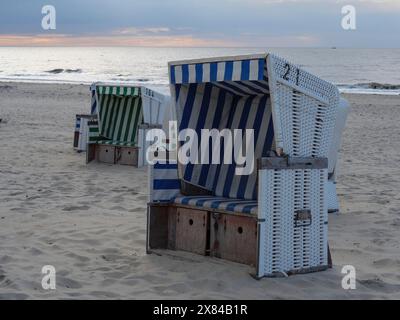 Sedie da spiaggia vuote con motivo a strisce blu-bianco e verde-bianco, in piedi su una spiaggia sabbiosa all'alba con vista sul mare, colorate sedie da spiaggia Foto Stock