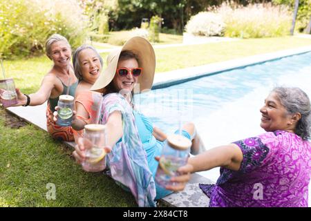 Incontro all'aperto con diverse amiche anziane che si godono un drink a bordo piscina Foto Stock