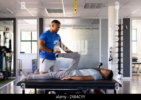 Presso il centro di riabilitazione, fisioterapista birazziale maschile e paziente che assiste con esercizi alle gambe Foto Stock