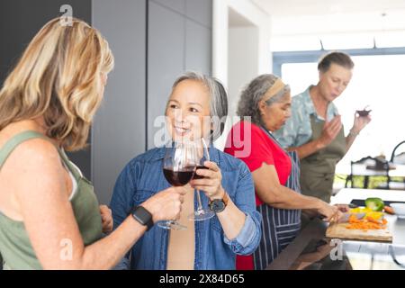 Diverse amiche anziane si riuniscono in cucina a casa, chiacchierano e cucinano Foto Stock