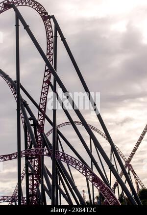 Schema astratto realizzato da Roller Coaster al parco a tema Village Roadshow, Gold Coast, Australia. Acciaio viola che torce e gira contro il cielo grigio. Foto Stock