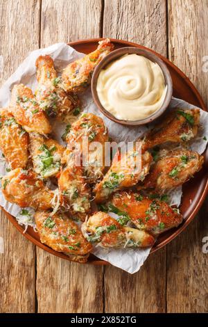 Le ali di parmigiano di pollo sono cotte al forno o fritte ad aria e poi ricoperte in una salsa di parmigiano all'aglio al bufala sul piatto del tavolo. Verticale in alto Foto Stock