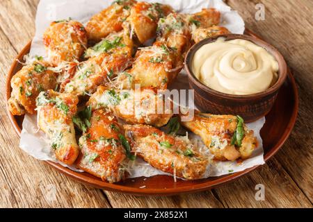 Ali di pollo al burro di parmigiano classico all'aglio servite con maionese da vicino in un piatto sul tavolo. Orizzontale Foto Stock