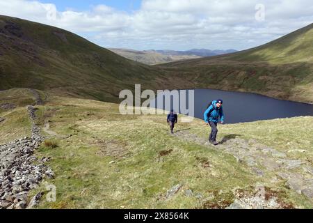 Due uomini (escursionisti) camminando lungo il Wainwright 'Fairfield' da Grisedale Hause sopra Grisedale Tarn nel Lake District National Park, Cumbria, Inghilterra Foto Stock