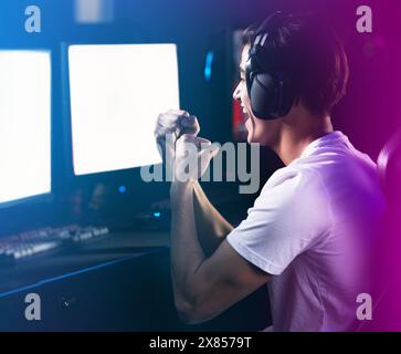 Neon, uomo e festeggiamenti come videogamer professionista con schermo per computer per videogiochi online ed entusiasmante. Cuffie, eSport e felici a casa con la vittoria Foto Stock