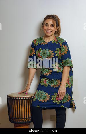 Il ritratto di una donna latina adulta indossa un abito in stile africano e sta in piedi accanto al tamburo djembe. Felice riposo dopo aver suonato durante un professionista religioso Foto Stock