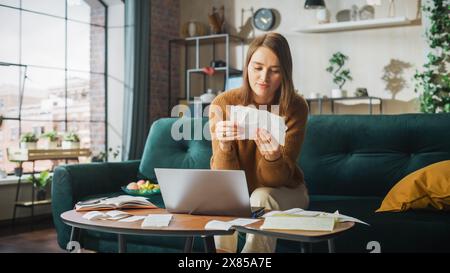 Happy Accounting a casa: Donna allegra e sorridente che utilizza un computer portatile, compilando i moduli fiscali. Donna d'affari che risolve tutti i suoi problemi burocratici, finisce il lavoro: Bollette, fatture, ha successo finanziario Foto Stock