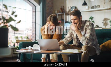 Stressante e drammatico contabilità a casa: Coppia con computer portatile e divano nell'appartamento. Young Family che compila moduli fiscali, documenti ipotecari, bollette, assegni, saldi, le fatture sono in ordine Foto Stock