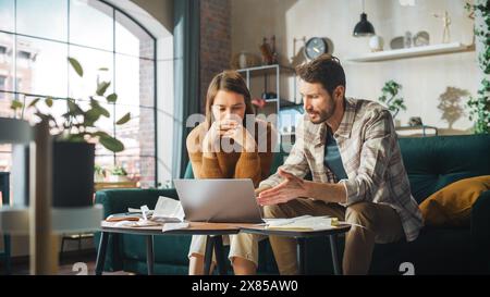 Contabilità a casa: Coppia con computer portatile, consulenza in appartamento. Young Family che compila moduli fiscali, documenti ipotecari, bollette, assegni, saldi, le fatture sono in ordine Foto Stock